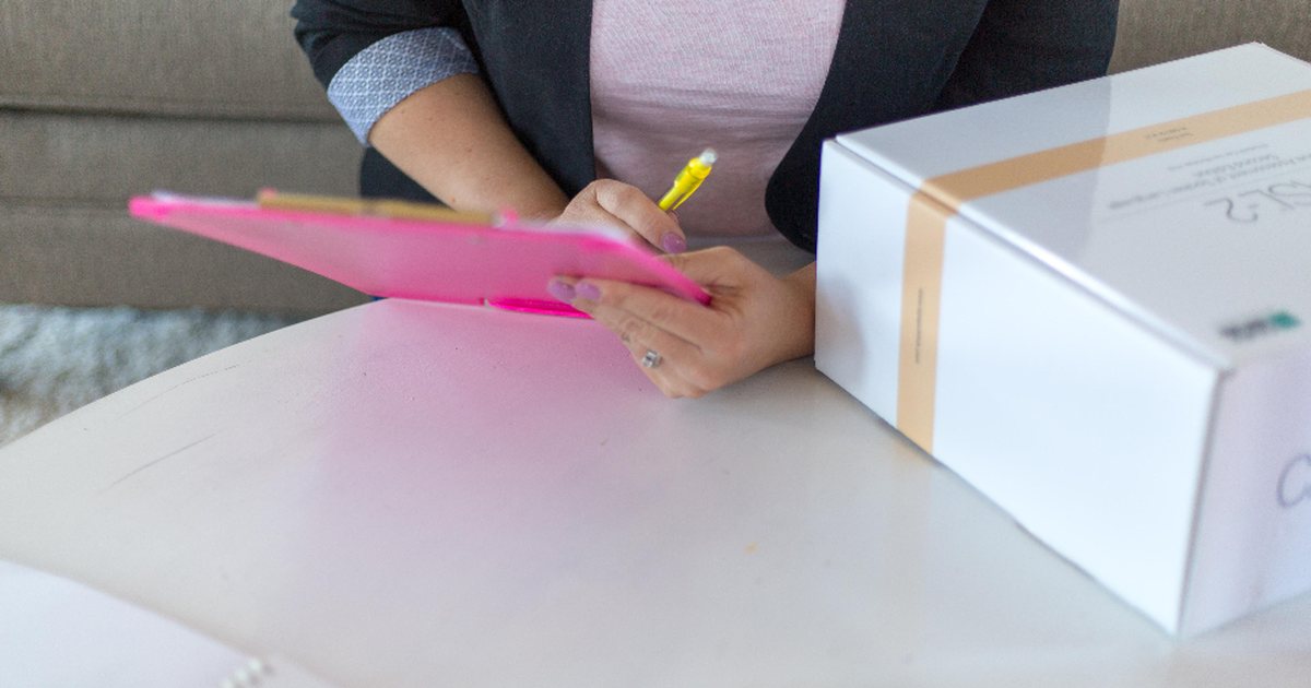 Persona escribiendo con un rotulador rosa sobre un portapapeles