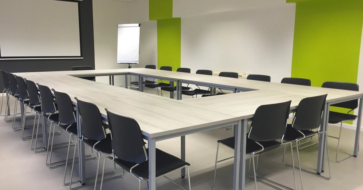 Sala de reuniones vacía con una mesa ovalada y sillas verdes
