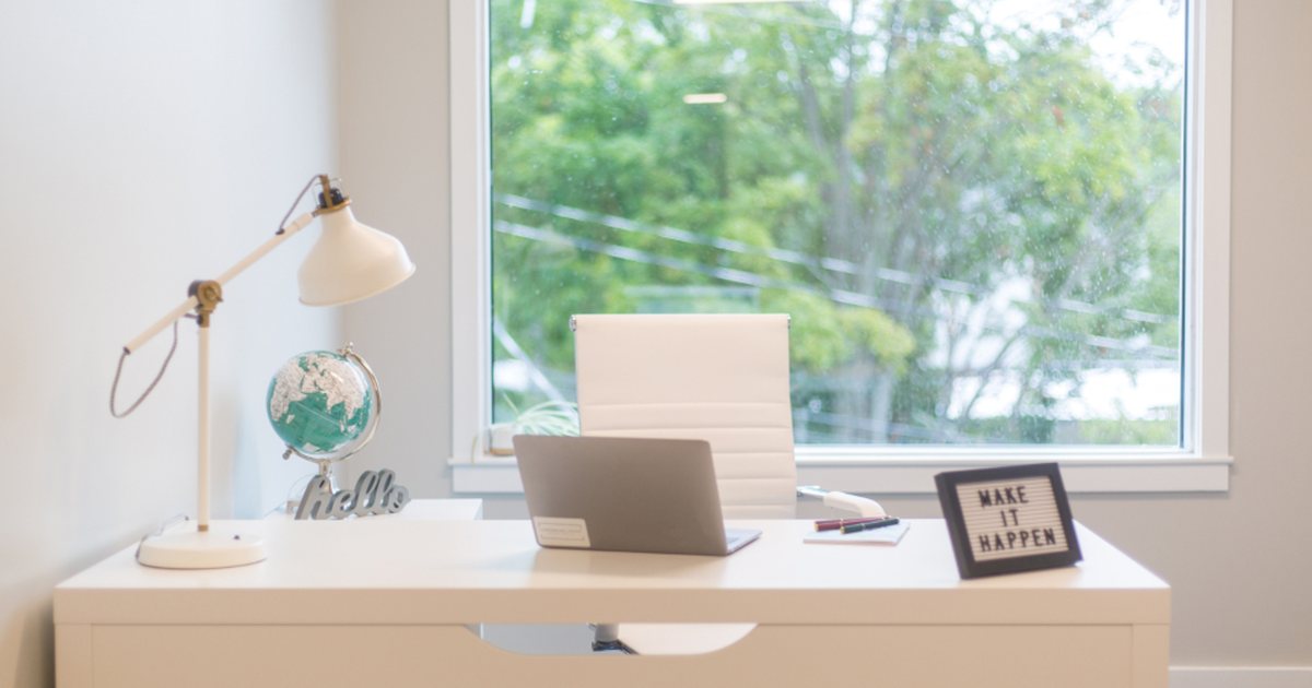 Escritorio de oficina en casa minimalista junto a una ventana, con lámpara y una silla