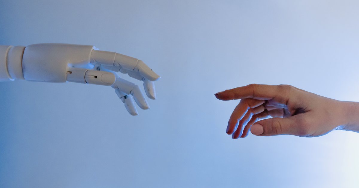 Una mano robótica articulada y una mano humana a punto de tocarse sobre un fondo azul, evocando el encuentro entre la inteligencia artificial y las personas.