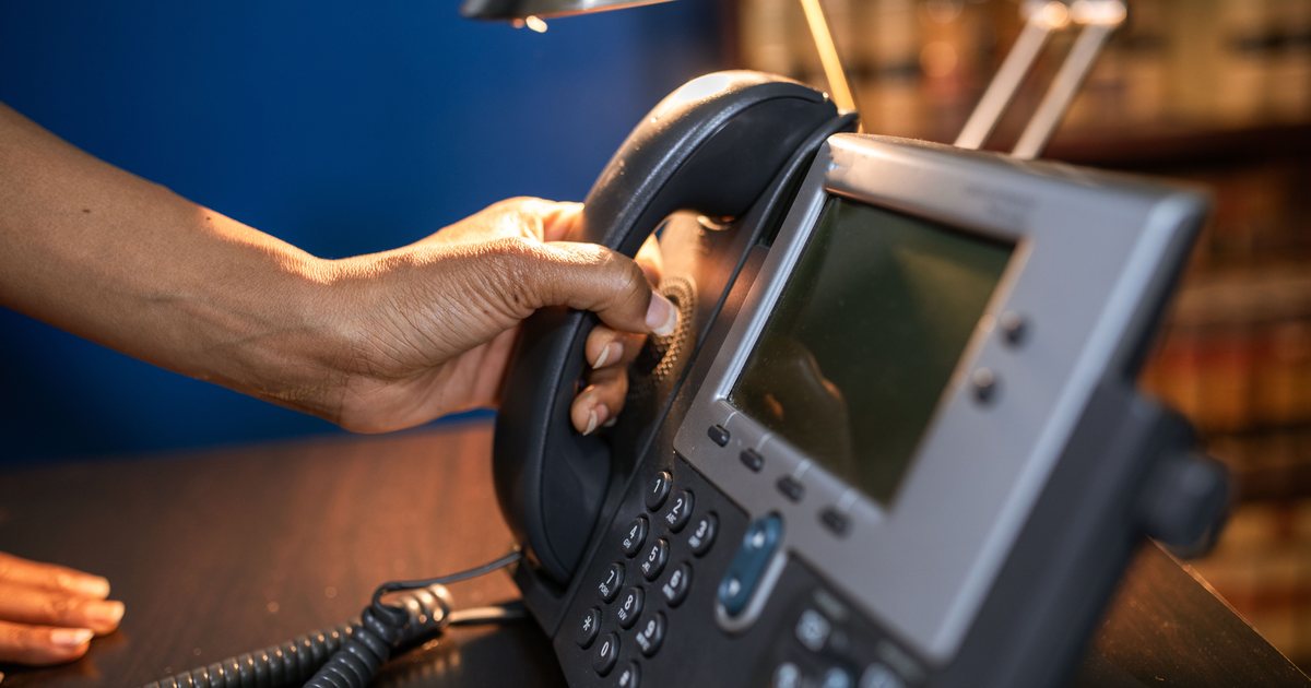 Mano descolgando el teléfono de una centralita de oficina