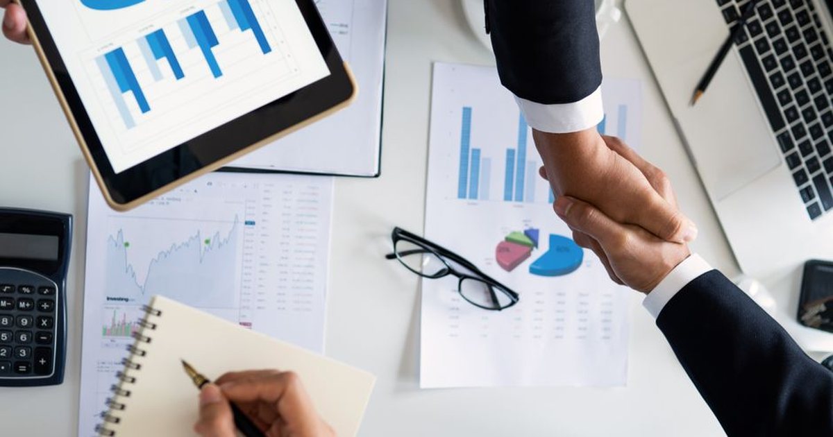 Manos estrechándose sobre una mesa con documentos y gráficos, vista cenital