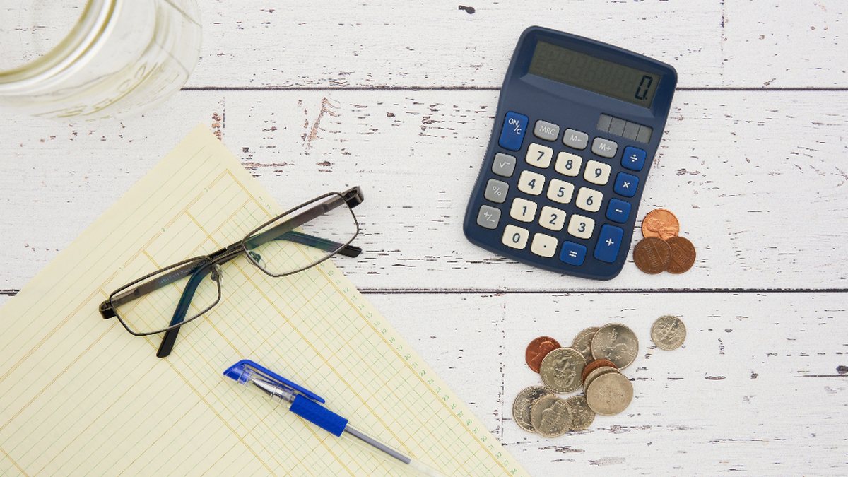 Calculadora, gafas y monedas sobre una mesa de madera