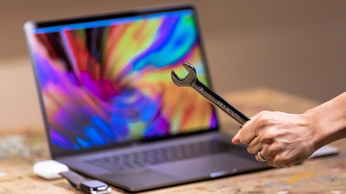 Hand holding a wrench in front of an open laptop