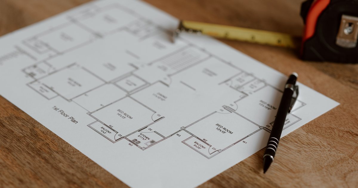 Plano arquitectónico de una vivienda extendido sobre una mesa de madera, junto a un lápiz y una cinta métrica.