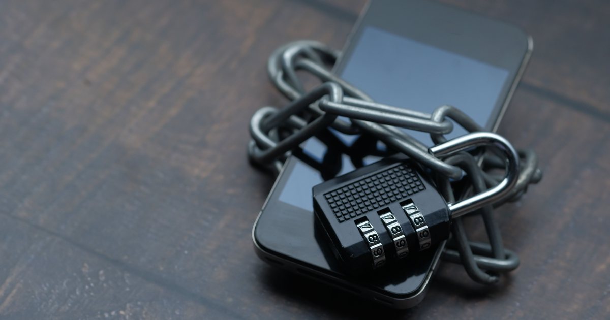 Un teléfono móvil envuelto con una cadena metálica y cerrado con un candado de combinación, sobre una mesa de madera oscura.