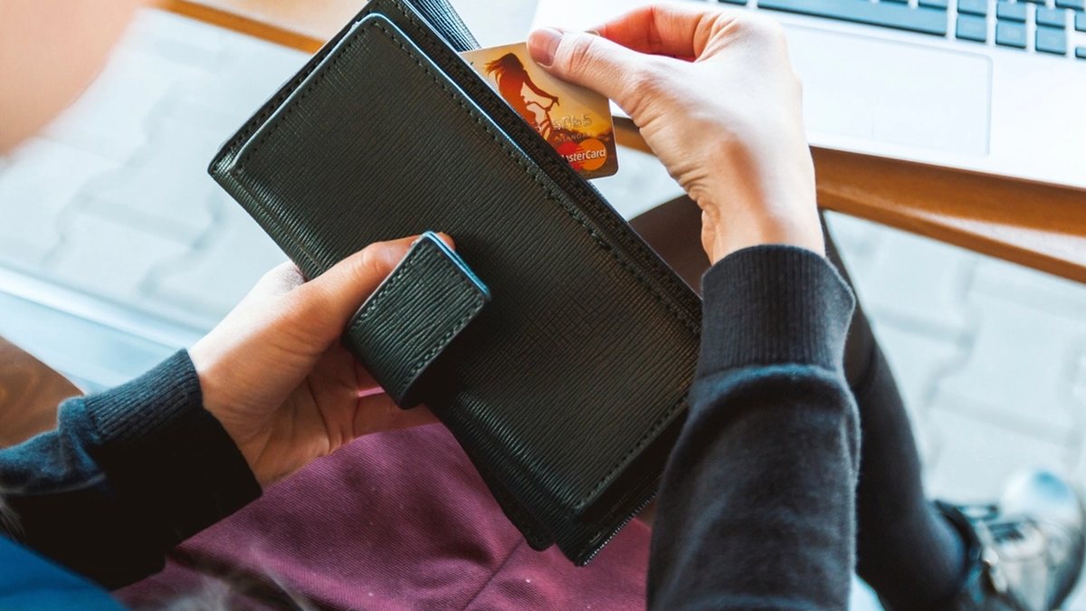 Mano sacando una tarjeta de crédito de una cartera junto a un portátil