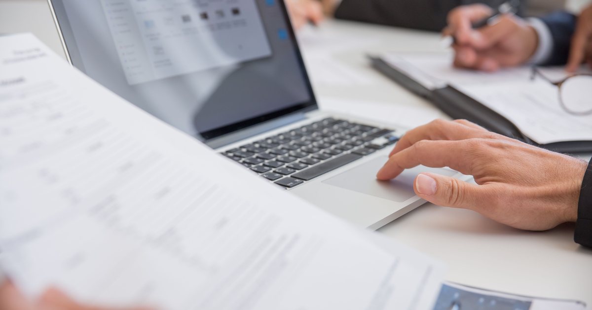 Manos sobre un portátil junto a documentos impresos en una mesa de reunión