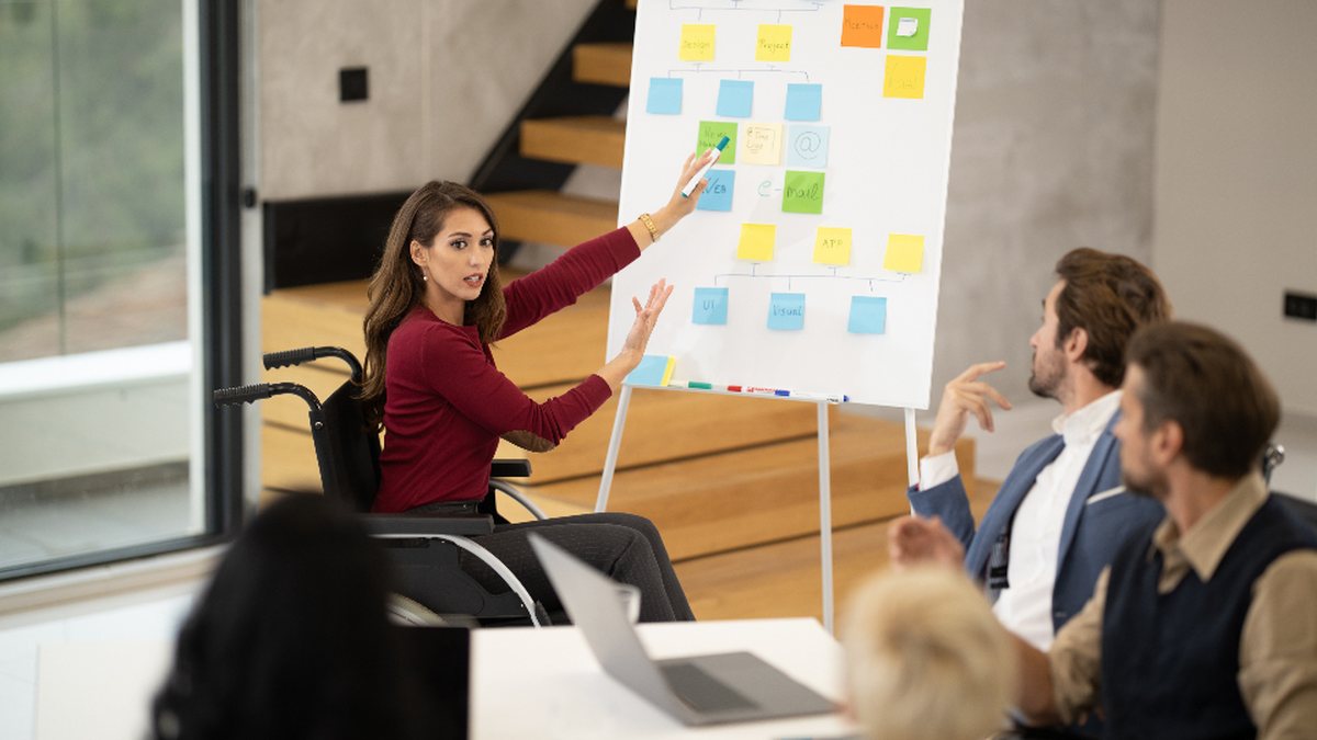 Mujer en silla de ruedas liderando una presentación ante su equipo