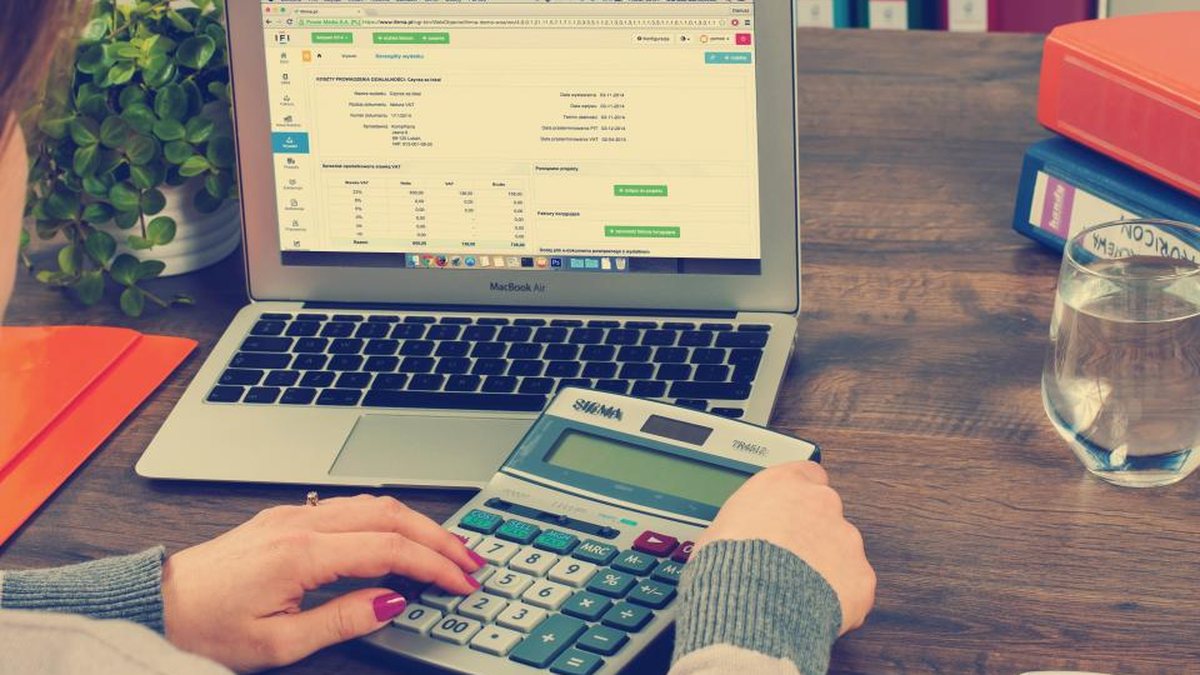 Persona usando una calculadora junto a un portátil con una hoja de cálculo
