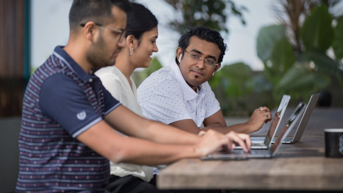 Tres compañeros trabajando juntos en portátiles al aire libre