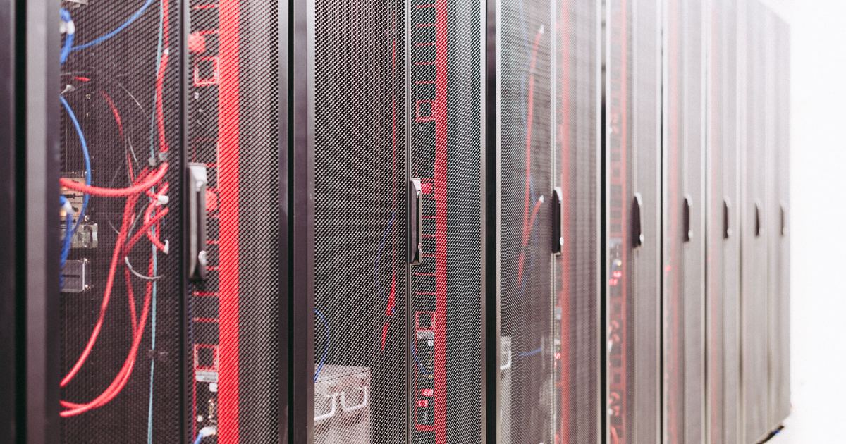Pasillo de un centro de datos con varios racks de servidores en fila y cableado de red rojo y azul visible tras las puertas perforadas