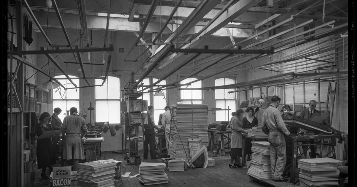 Interior de una nave industrial con trabajadores y maquinaria, en blanco y negro