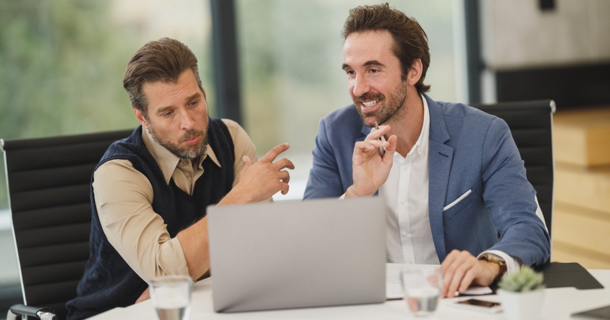 Dos hombres conversando y mirando la pantalla de un portátil en una reunión de trabajo