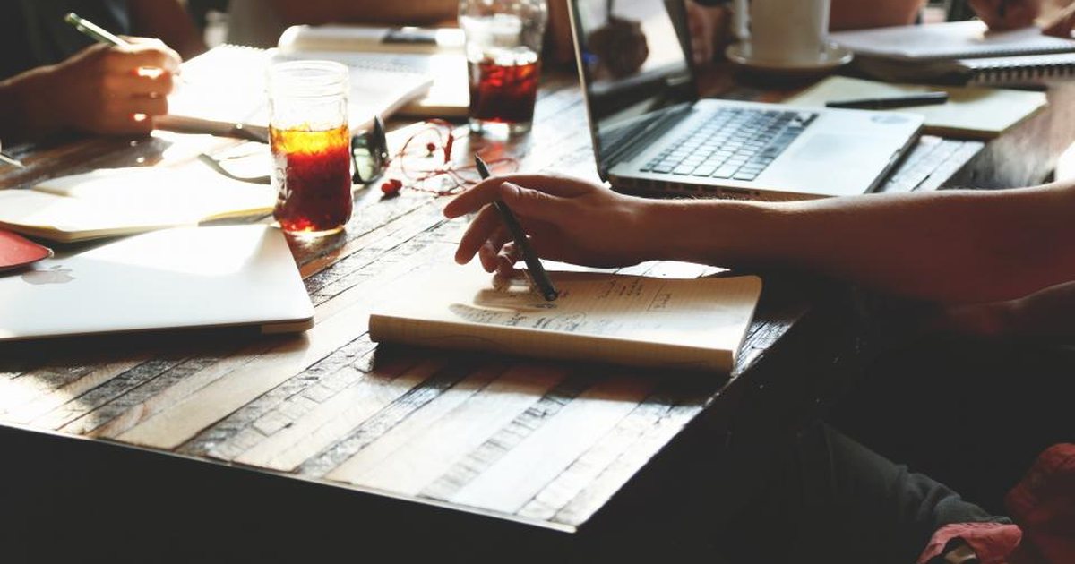 Personas trabajando en equipo alrededor de una mesa con portátiles y cuadernos
