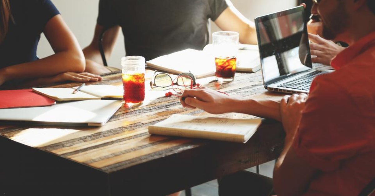 Personas trabajando alrededor de una mesa con portátiles y cuadernos